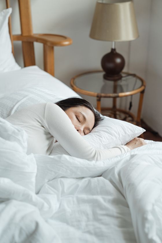 Seen from above, a person sleeping peacefully on pale bedding in early morning light. Photo by Ketut Subiyanto on Pexels.