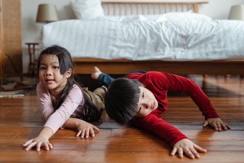 Happy little siblings playing on floor near bed