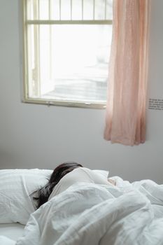 一名妇女在阳光明媚的卧室里安详地睡着，卧室里铺着柔软的床上用品，挂着窗帘