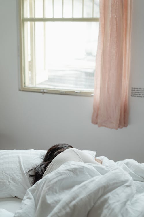 Free Woman Lying on Bed Near Window Stock Photo