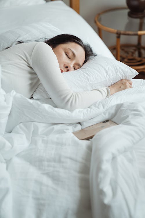 Woman in White Long Sleeved Shirt Lying on Bed