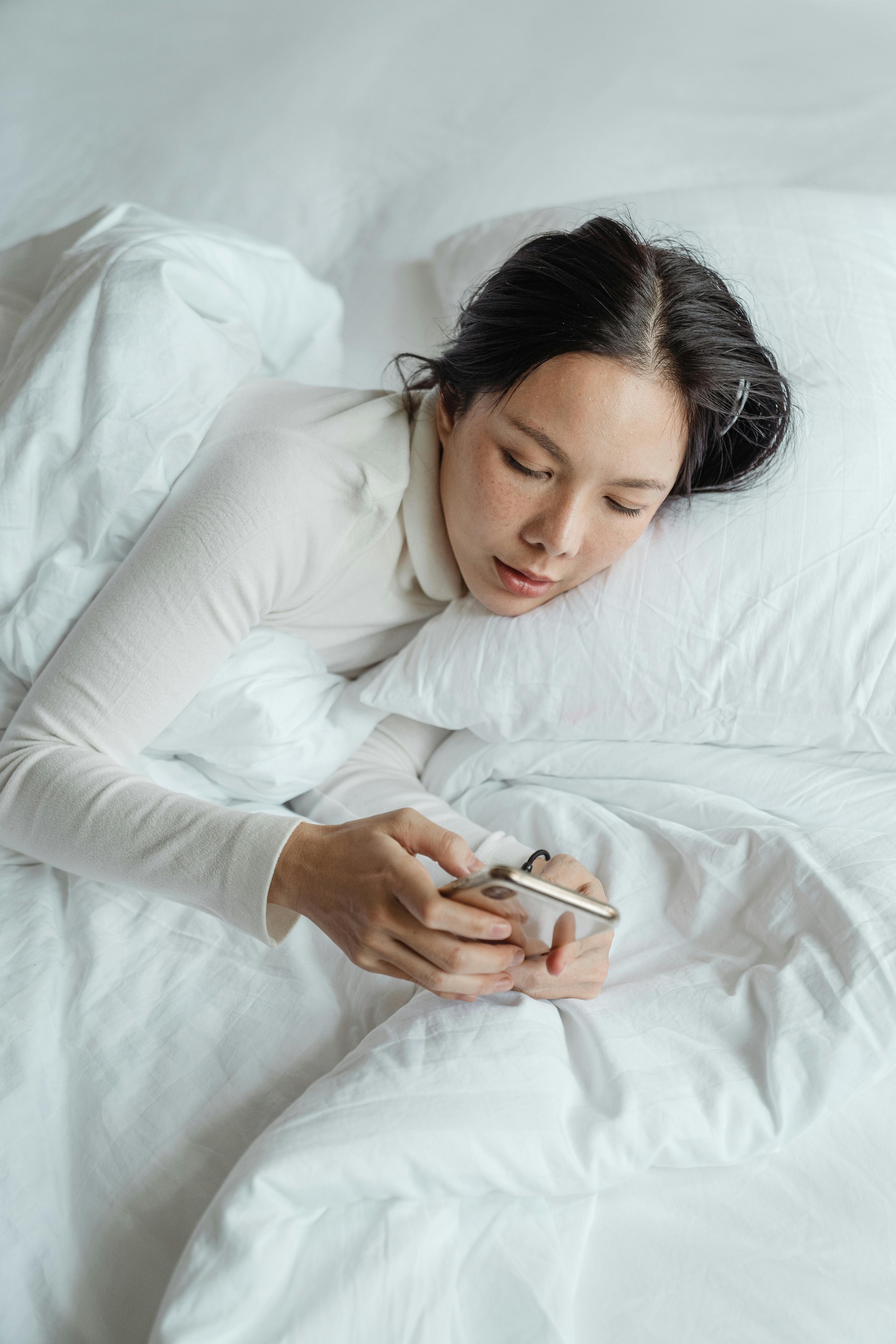 positive woman waking up and using smartphone in bed