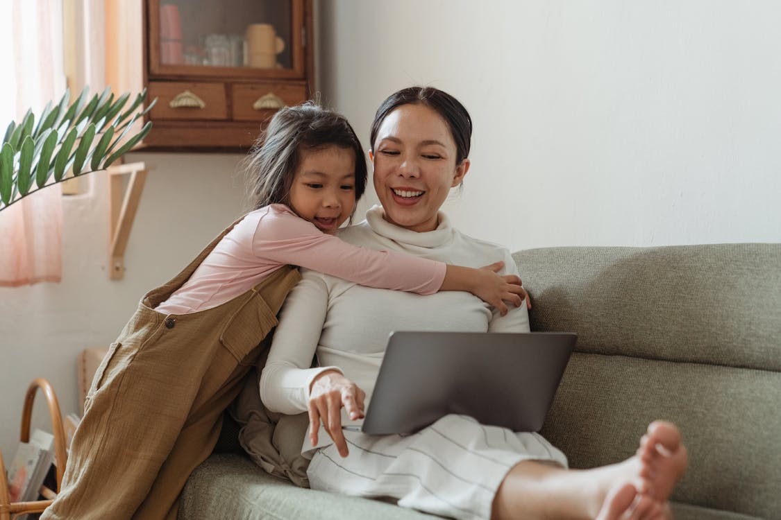 Free Cheerful girl hugging mother with laptop Stock Photo