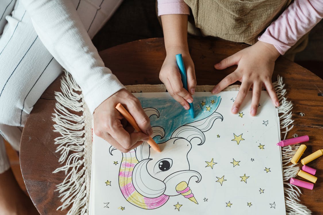 Crop kid with mother coloring picture of unicorn