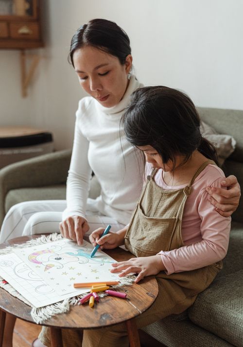 Free Concentrated Asian woman with adorable focused girl in casual clothes sitting at table and coloring picture together in daylight Stock Photo