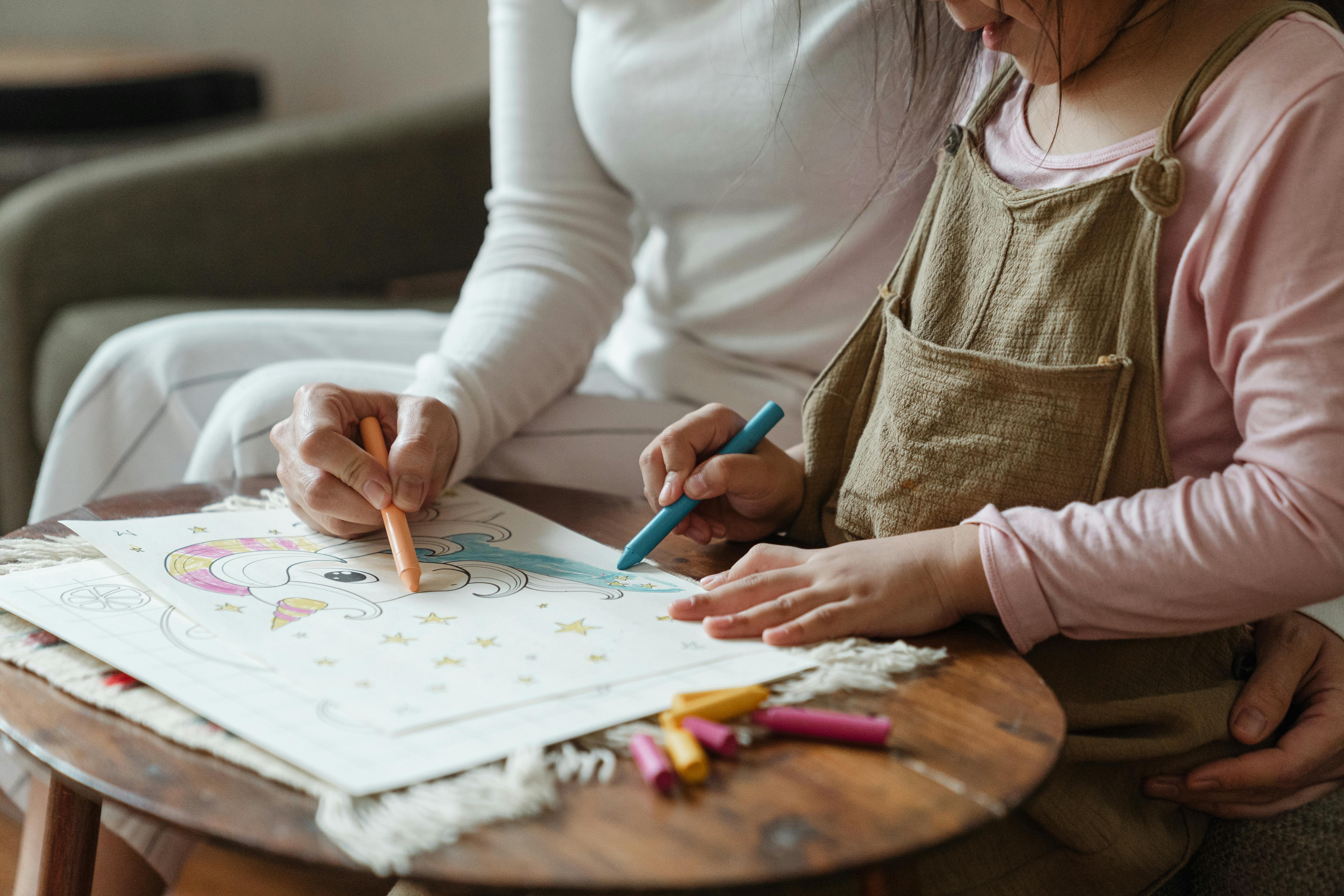 crop mother and daughter coloring drawing together on coffee table