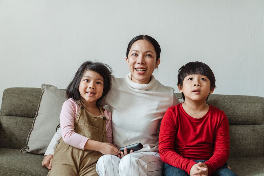 A mother and two children laughing on the couch while watching a home video