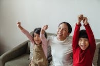 Cheerful ethnic mother and children watching game on TV sitting on sofa and celebrating winning