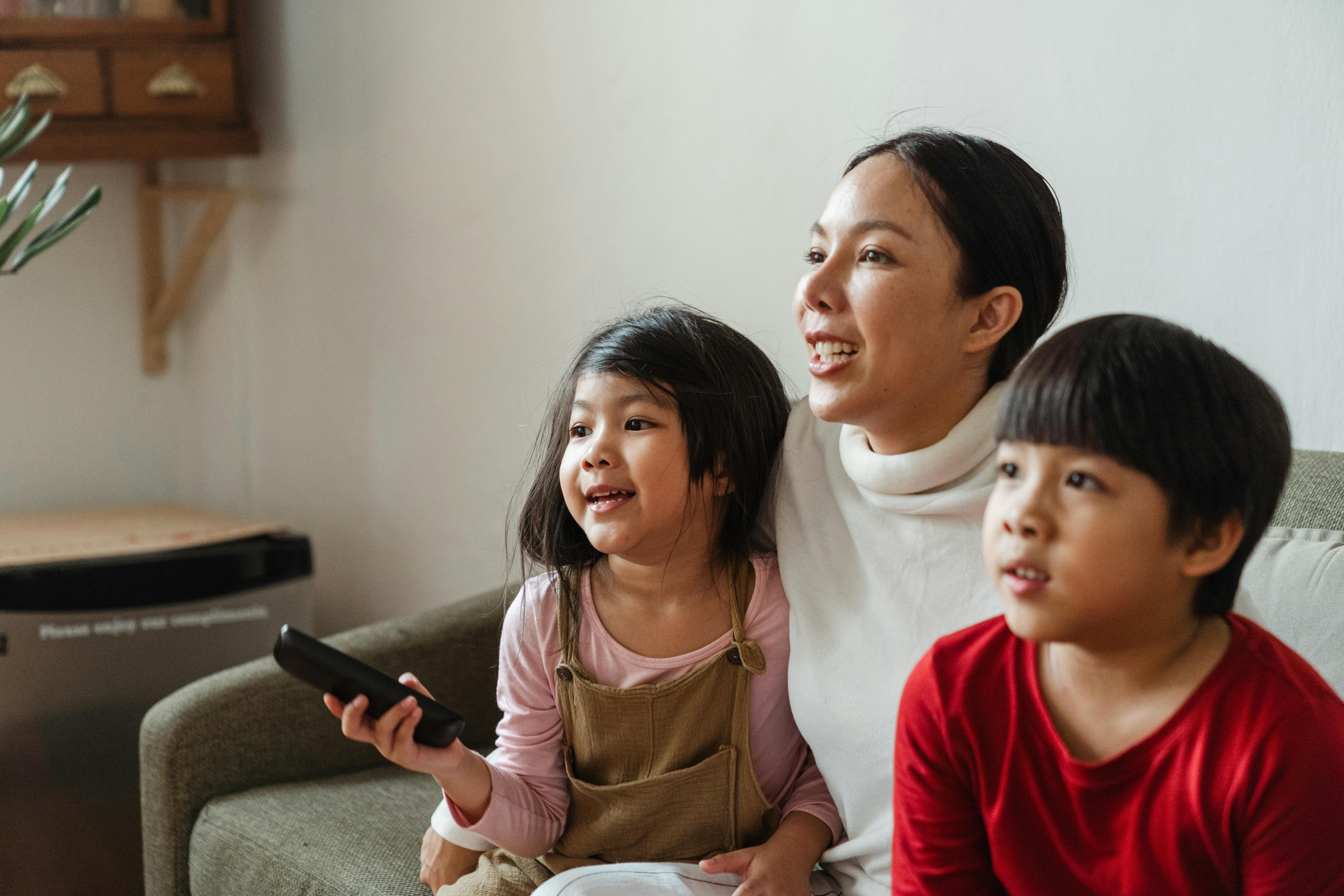adorable ethnic kids with mother watching tv on weekend