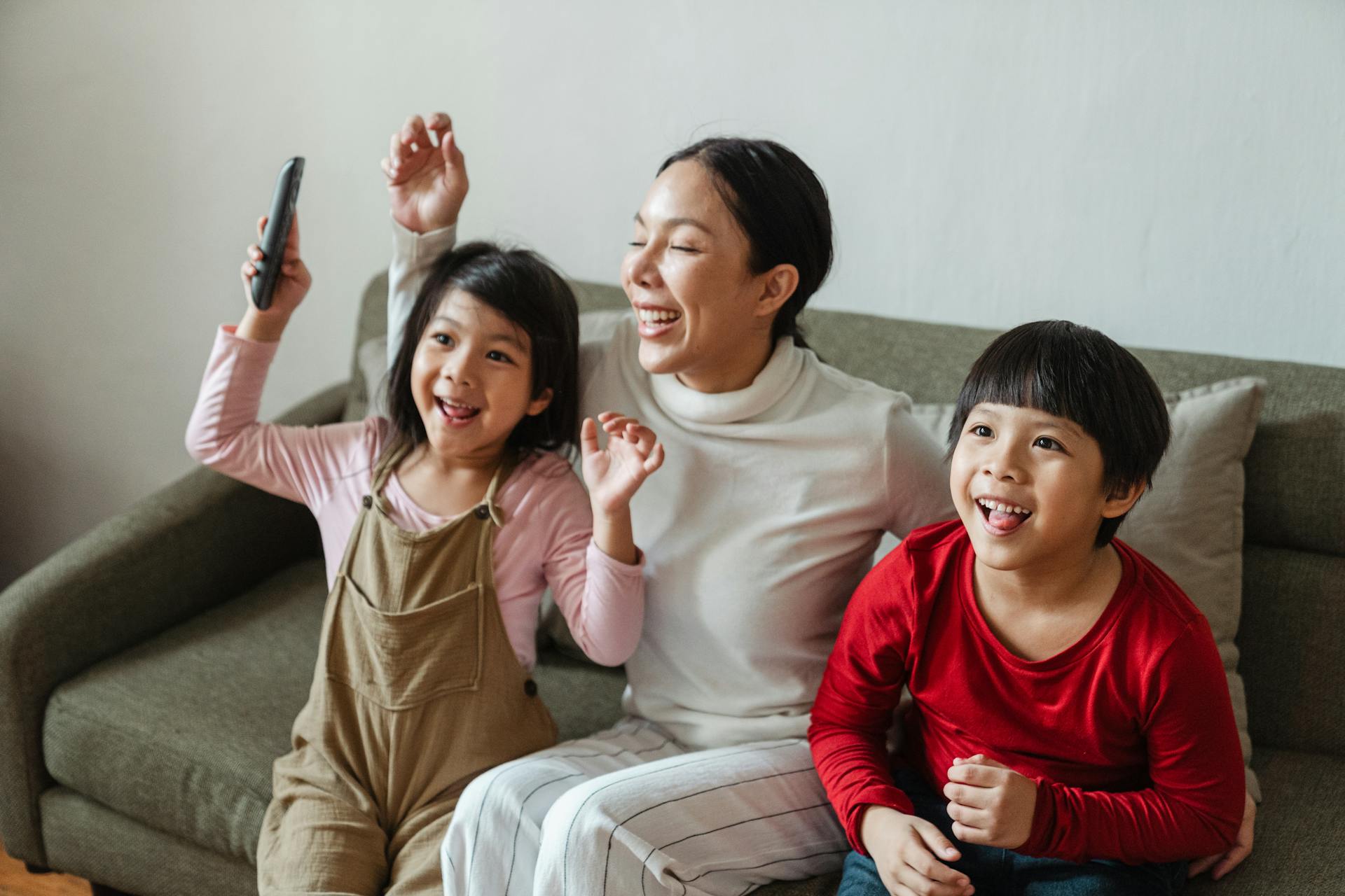 Excited young ethnic woman with kids watching funny cartoon on TV