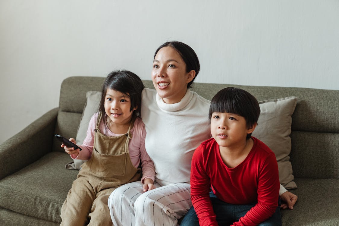 Happy young ethnic mother and little children watching TV on sofa
