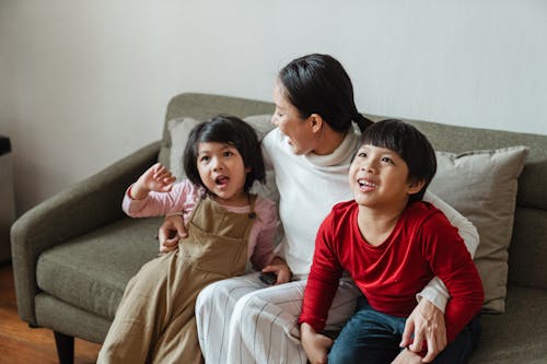From above of cheerful little ethnic children spending time together with mother and having fun sitting on sofa