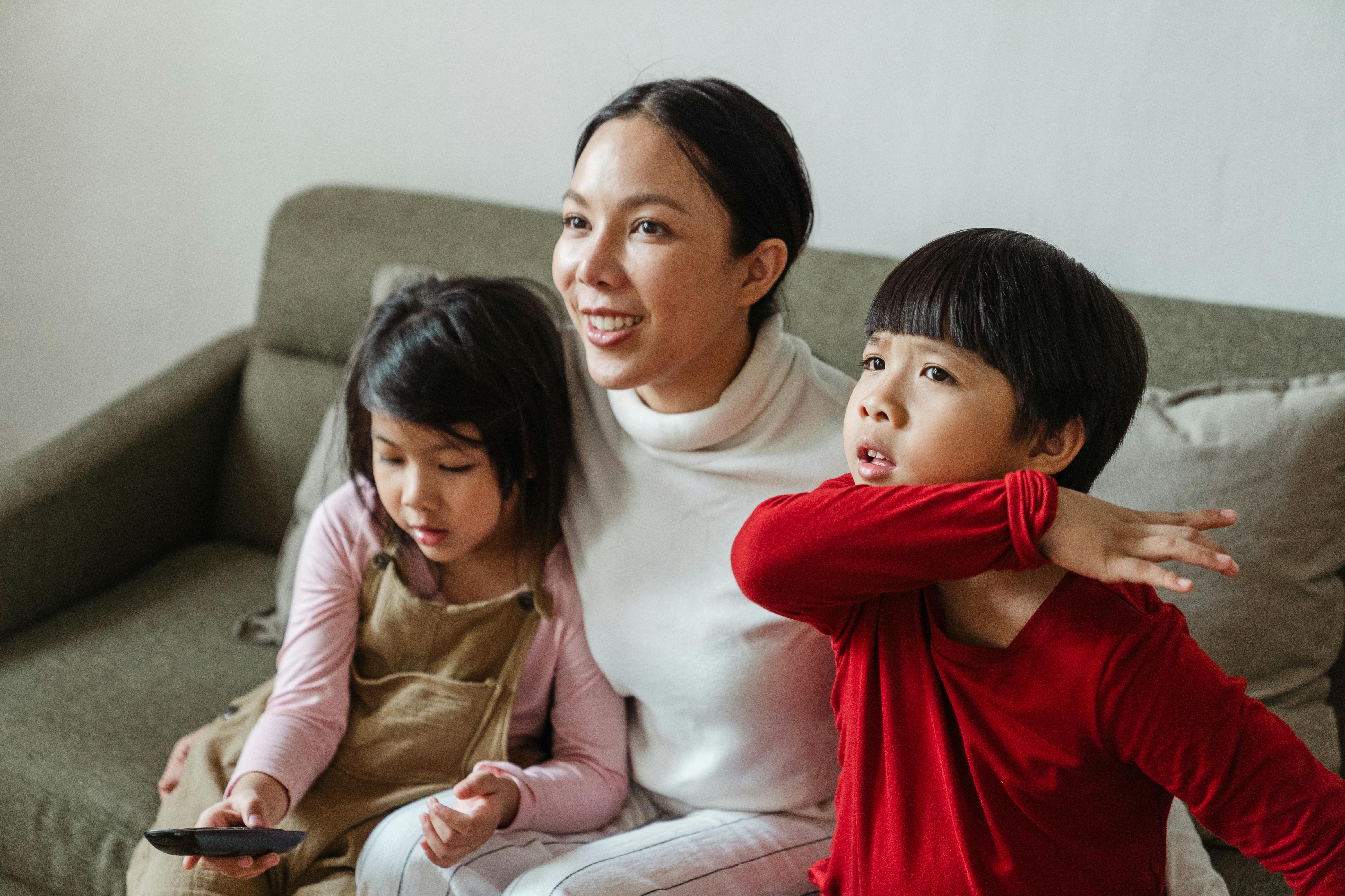 cute ethnic kids and mother sitting on sofa and watching tv with attention