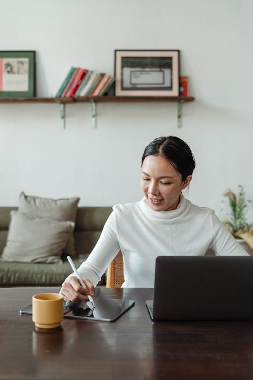 Young Asian female freelancer using gadgets while working at home