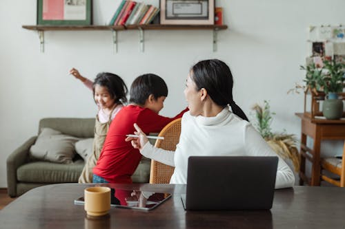 Free Young Asian working mother scolding little kids playing and making noise during remote job at home Stock Photo