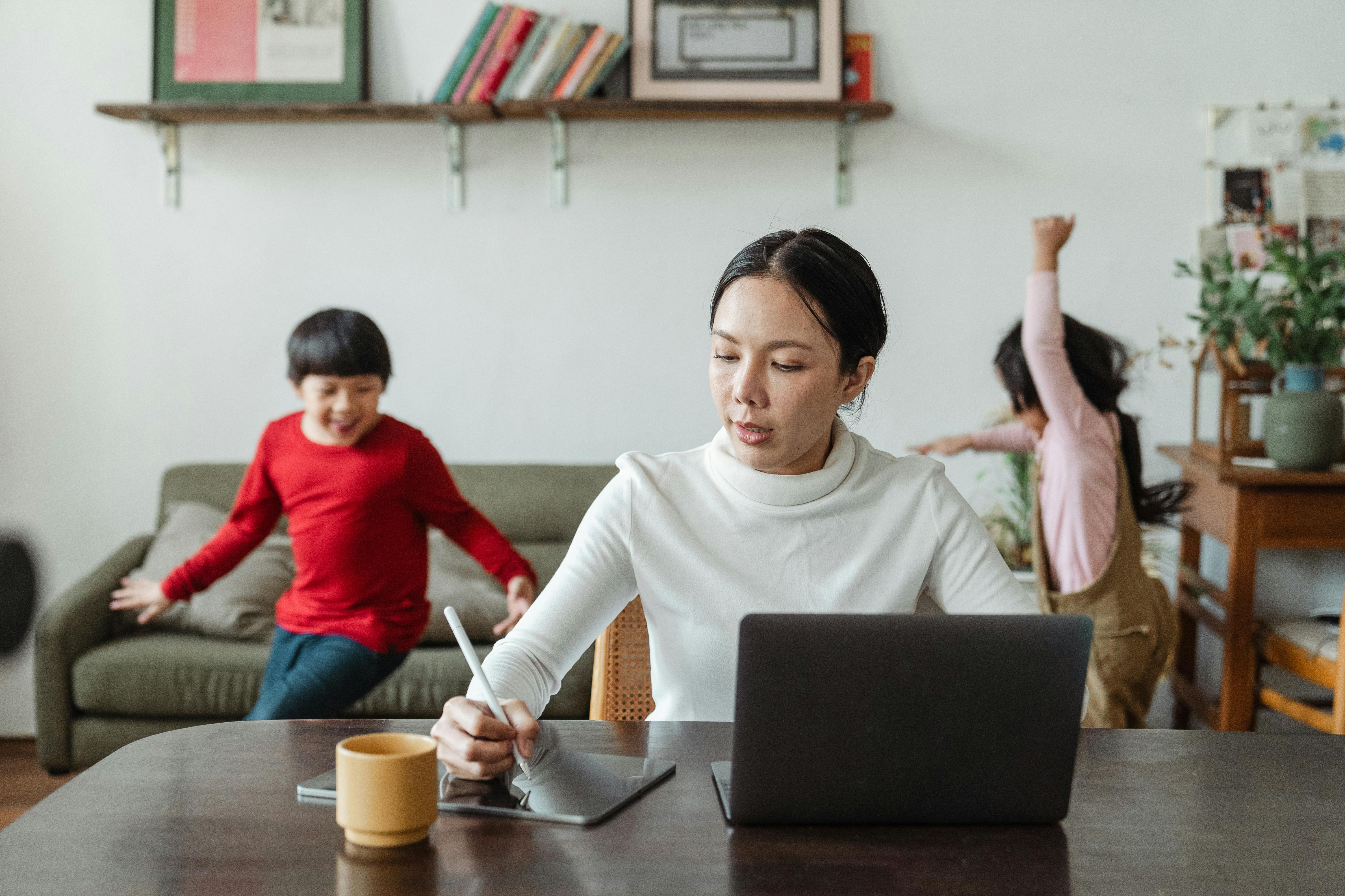 busy mom working on laptop and noisy children running around