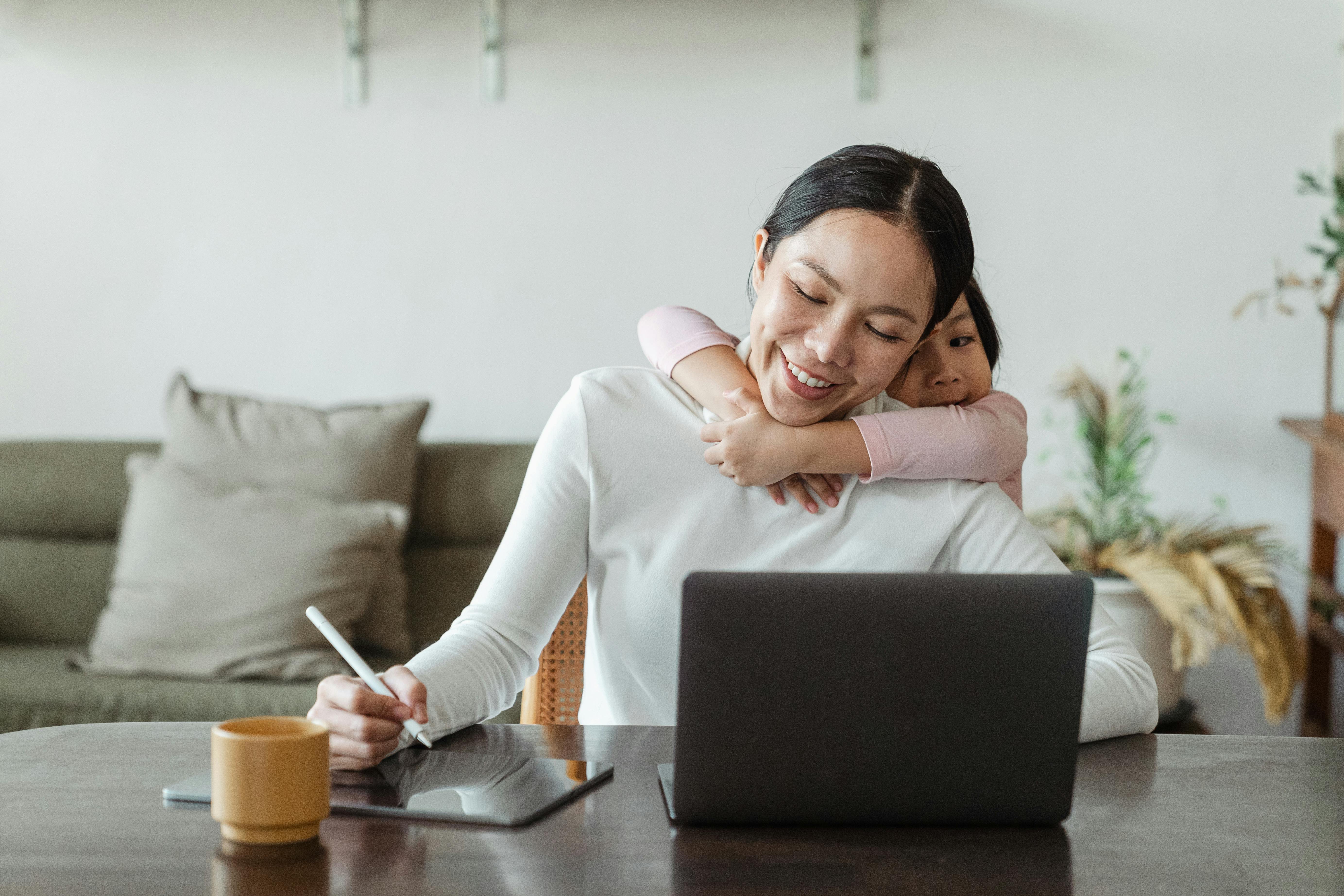 happy mother working from home and little daughter hugging mom