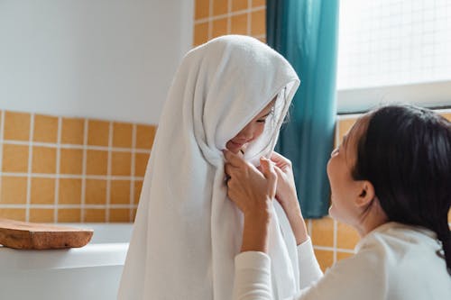 Free Cheerful ethnic mum wiping cute little daughter with big fluffy towel in modern bathroom at home Stock Photo