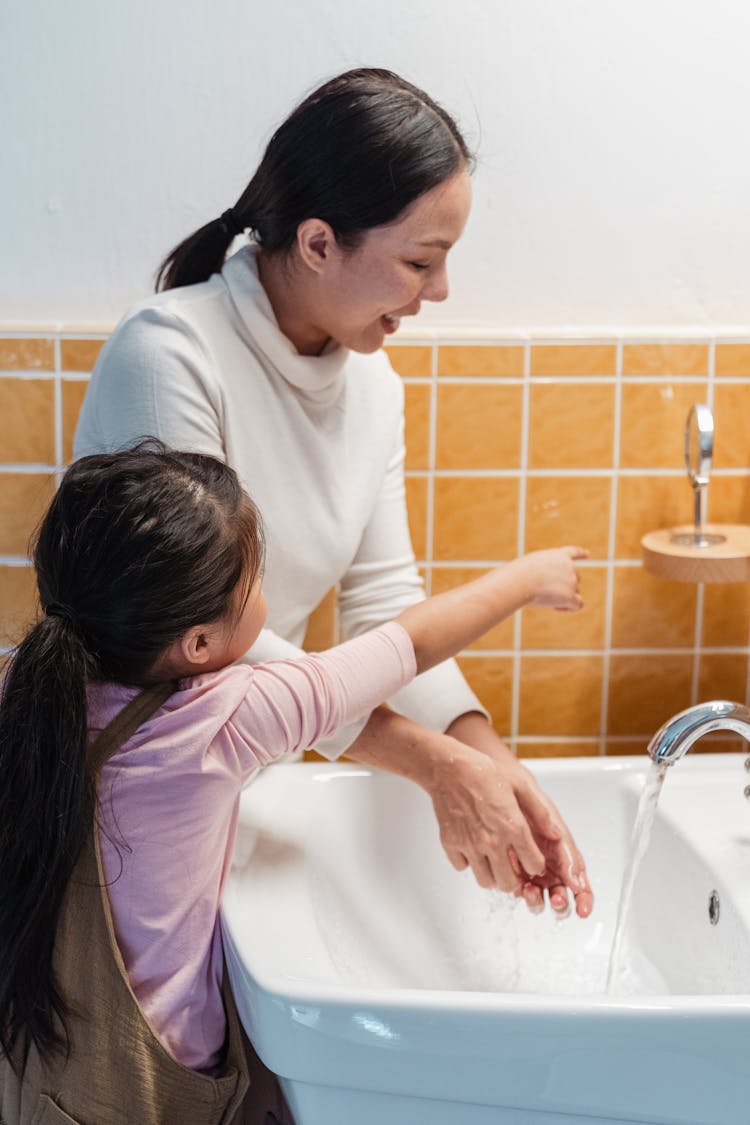 Ethnic Mother And Daughter Washing Hands Together In Bathroom