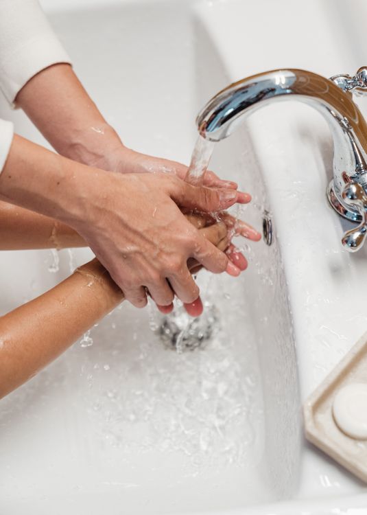 An adult helping a young child wash both hands under running water.