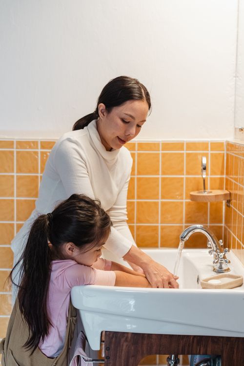 Mom teaching little daughter to wash hands properly