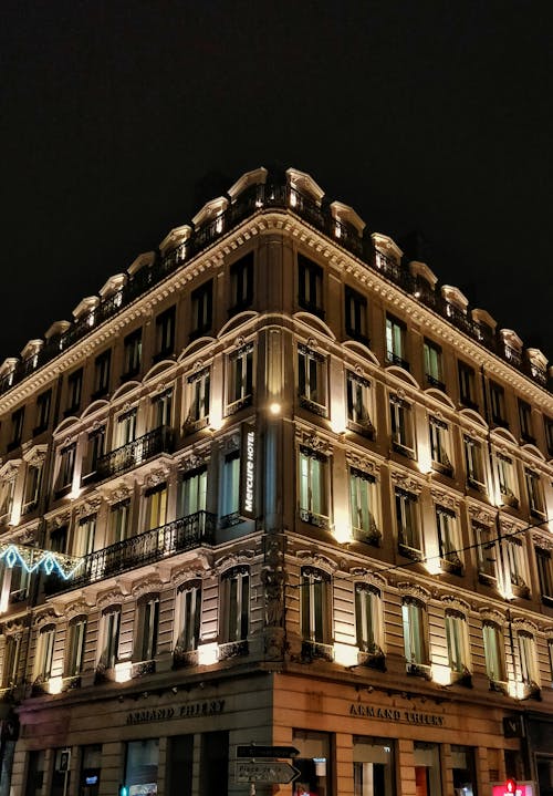 Low angle of corner of old fashioned building with illuminated exterior on background of dark sky at night in city