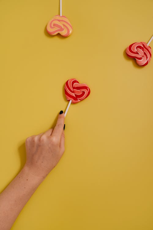 A Person Holding a Heart Shaped Lollipop on Yellow Background