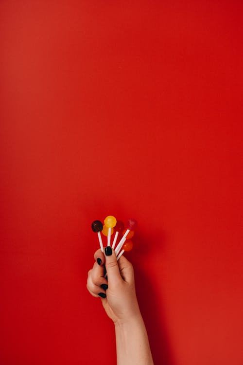 A Person Holding Different Colors of Lollipops on Red Background · Free  Stock Photo