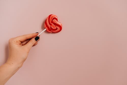 A Red Heart Shaped Lollipop on Light Pink Background