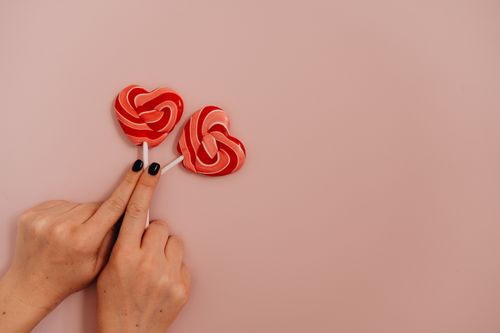 Free Hands holding red heart-shaped lollipops on a light pink background, symbolizing love. Stock Photo