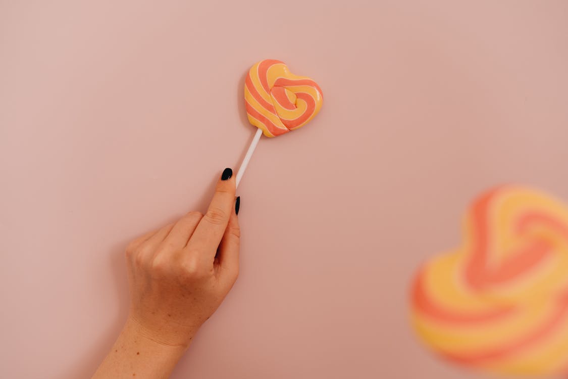 Person Holding Orange Heart Shaped Lollipop
