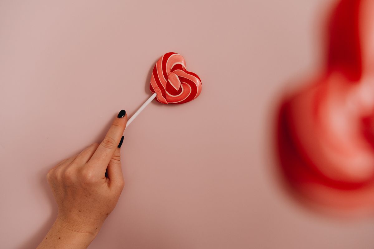 A hand holding a heart-shaped lollipop against a light pink background.