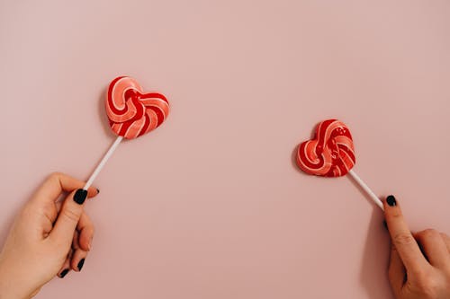 Person's Hands Holding Heart Shaped Lollipops
