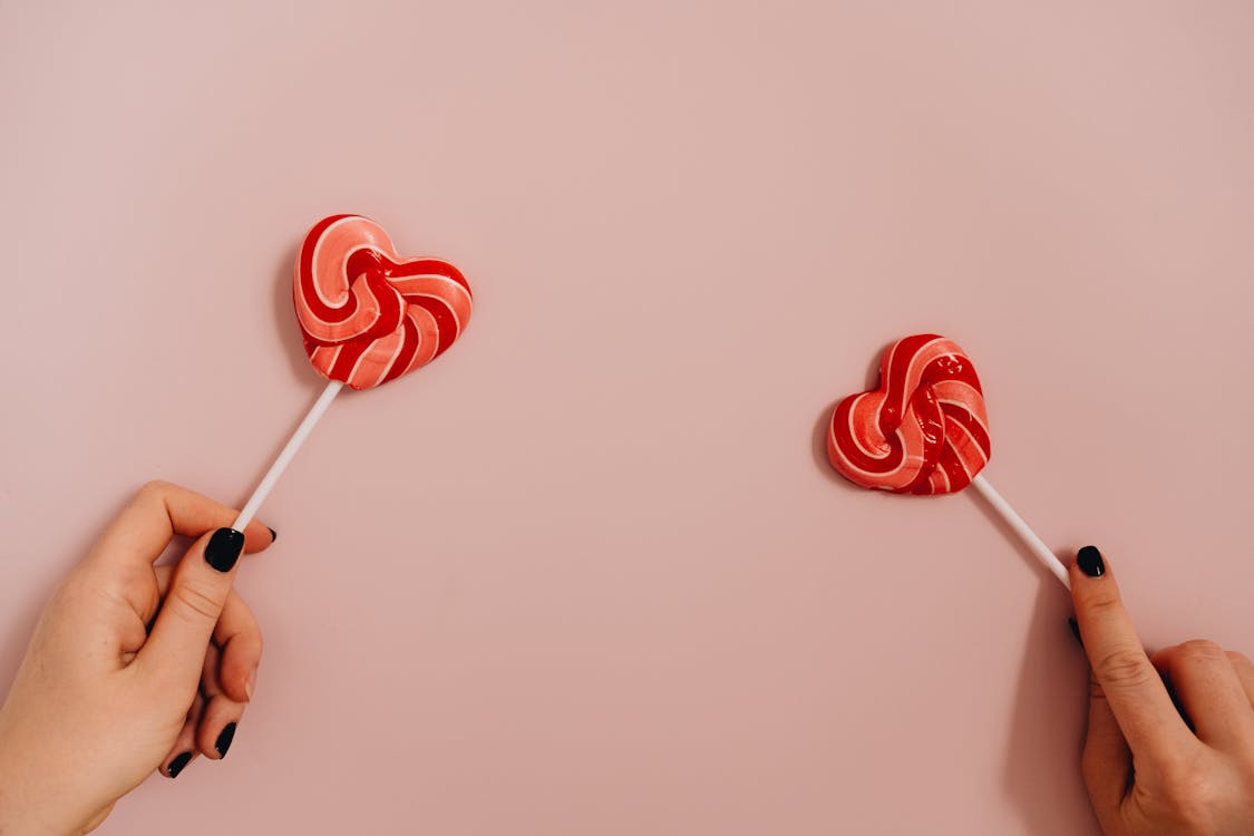 Person's Hands Holding Heart Shaped Lollipops