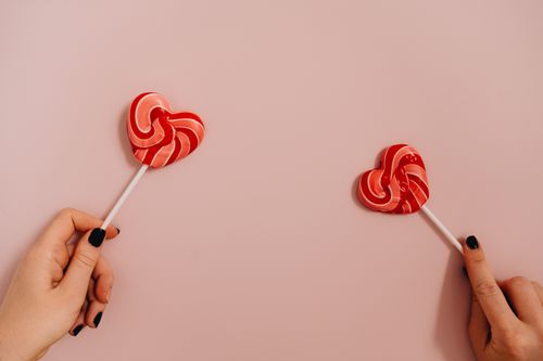 Free Two hands holding heart-shaped lollipops against a pastel pink background. Stock Photo