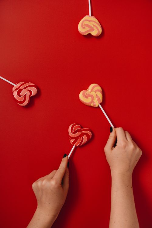 Free Colorful heart-shaped lollipops held by hands against a vivid red backdrop. Stock Photo