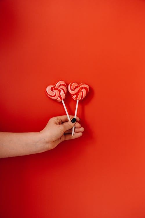 Person Holding Red Heart Shaped Lollipops