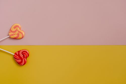 Free Two heart-shaped lollipops on a vibrant yellow and pink background, perfect for Valentine's Day themes. Stock Photo