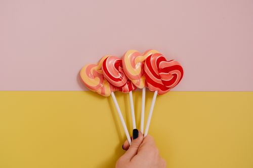 Free A hand holding vibrant heart-shaped lollipops against a pastel background. Stock Photo