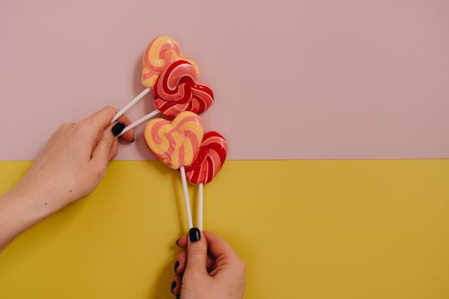 Free A pair of hands holding colorful heart-shaped lollipops against a pastel background. Stock Photo