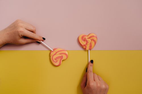 Free Close-up of hands holding heart-shaped lollipops on a pastel background. Stock Photo
