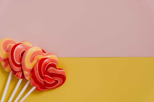 Free Heart-shaped, pink and yellow lollipops arranged on a vibrant background with copy space. Stock Photo