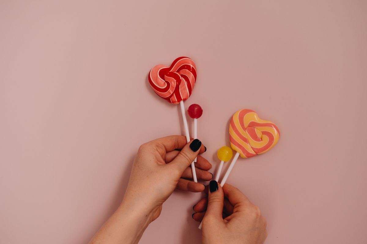 Close-up of hands holding colorful heart-shaped lollipops on a pink background.