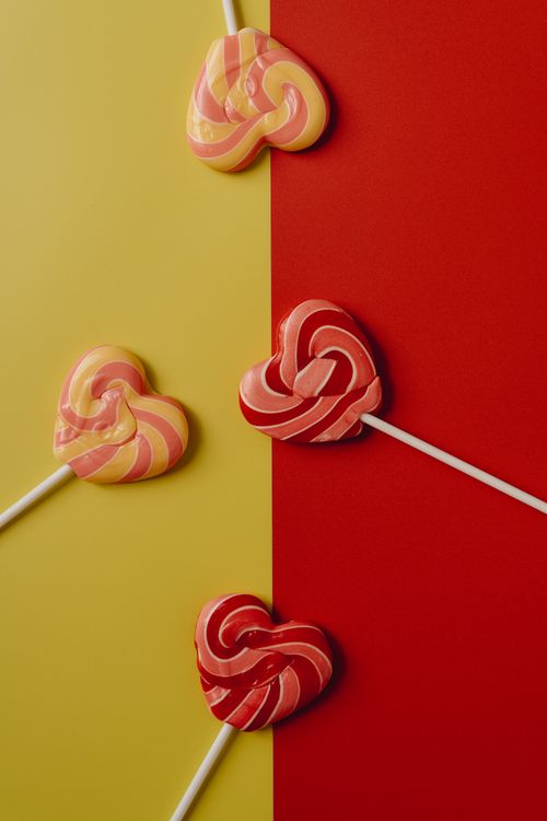 Free Heart-shaped lollipops on vibrant red and yellow background, perfect for candy-themed visuals. Stock Photo