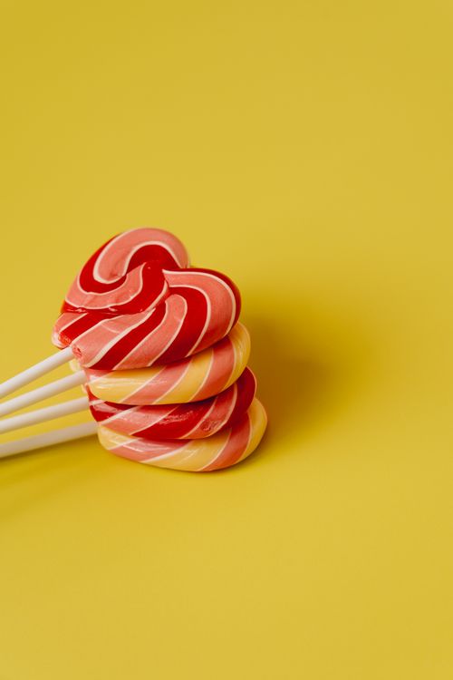 Free Close-up of spiral lollipops arranged on a bright yellow surface. Ideal for sweet and candy-themed visuals. Stock Photo