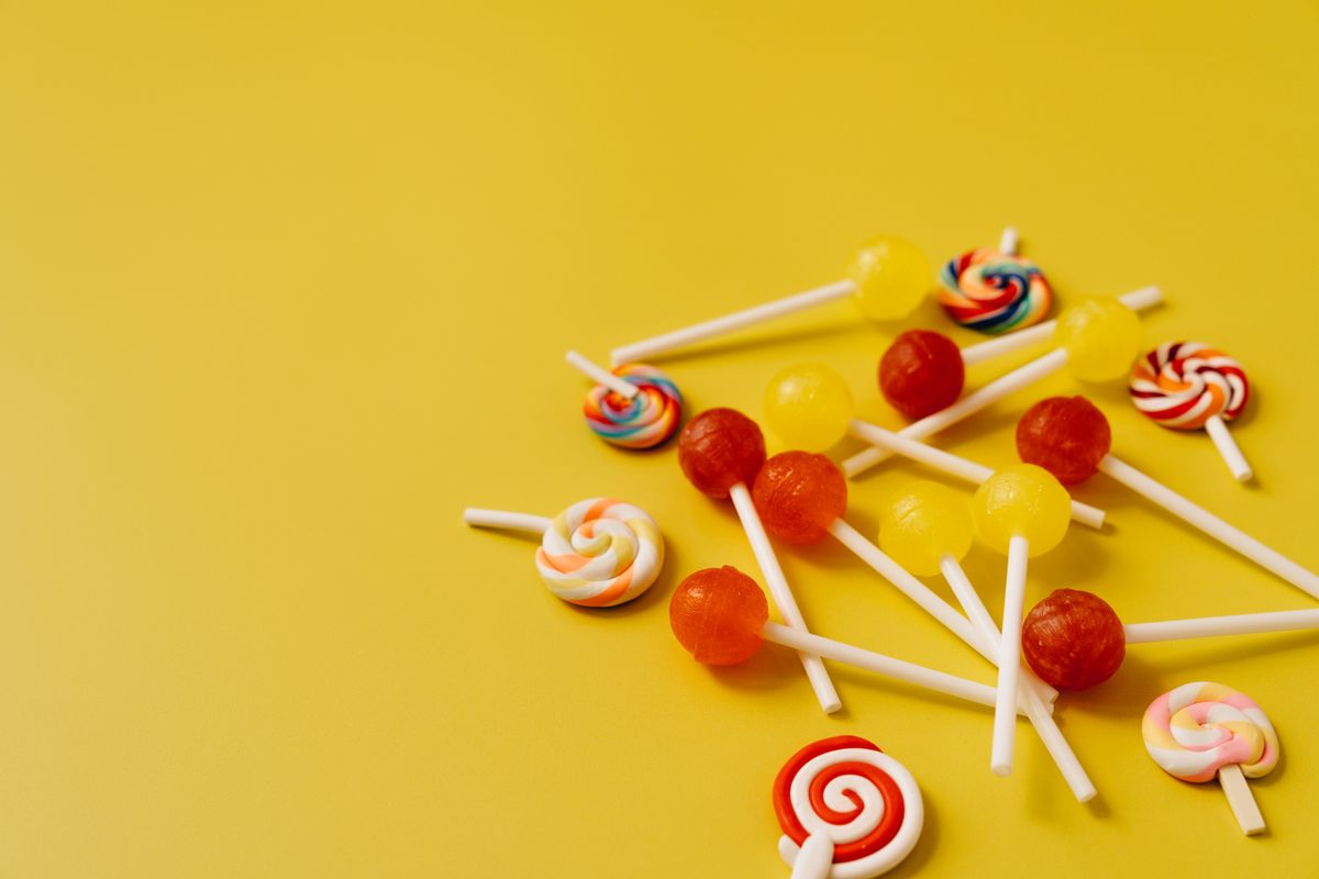 A close-up of colorful lollipops scattered on a bright yellow background with ample copy space.