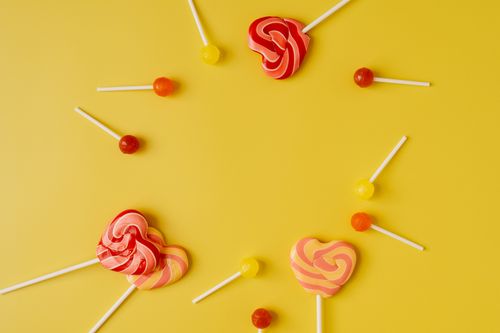 Free Bright and colorful heart-shaped lollipops arranged on a vibrant yellow background. Stock Photo