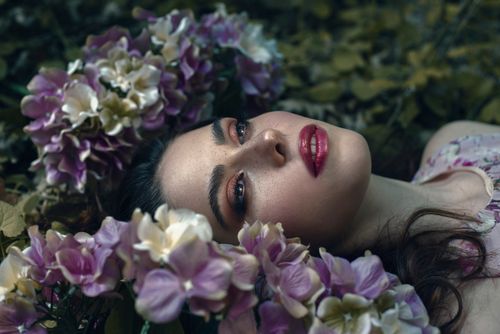 Free Portrait of a woman with red lips lying among purple and white flowers. Stock Photo