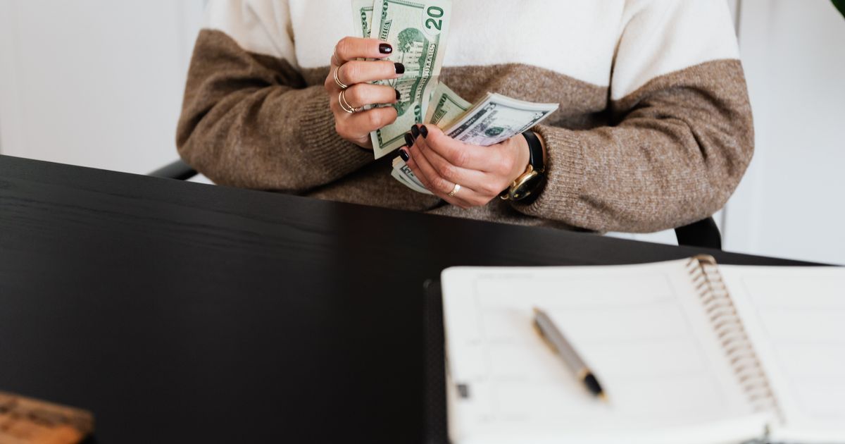 Close-up of an adult counting dollar bills at a desk with a notebook.