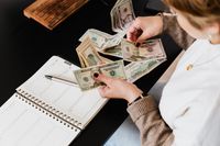 Hands counting banknotes beside an open ledger — photo by Kaboompics on Pexels